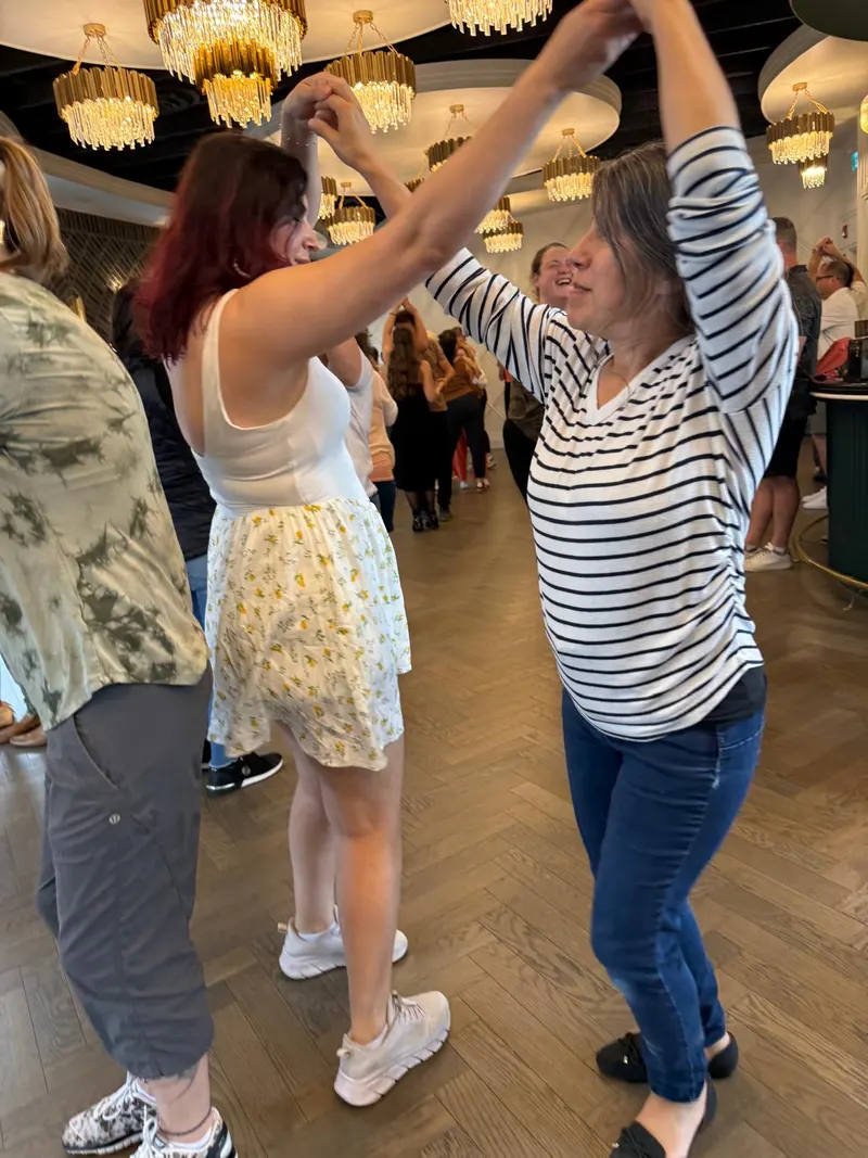 Two dancers with joined hands raised overhead, entering the sombrero move during a beginner merengue lesson in Chilliwack